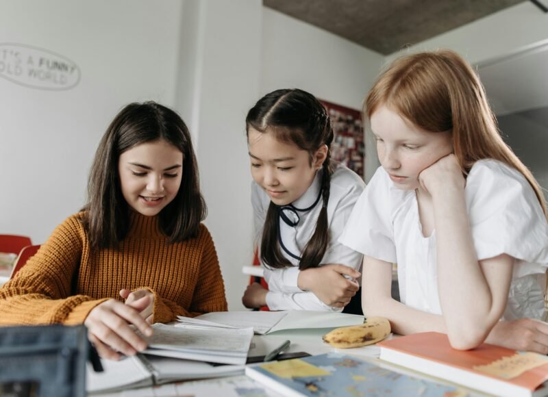 Three diverse schoolgirls working together over books in a classroom setting, fostering education and collaboration.